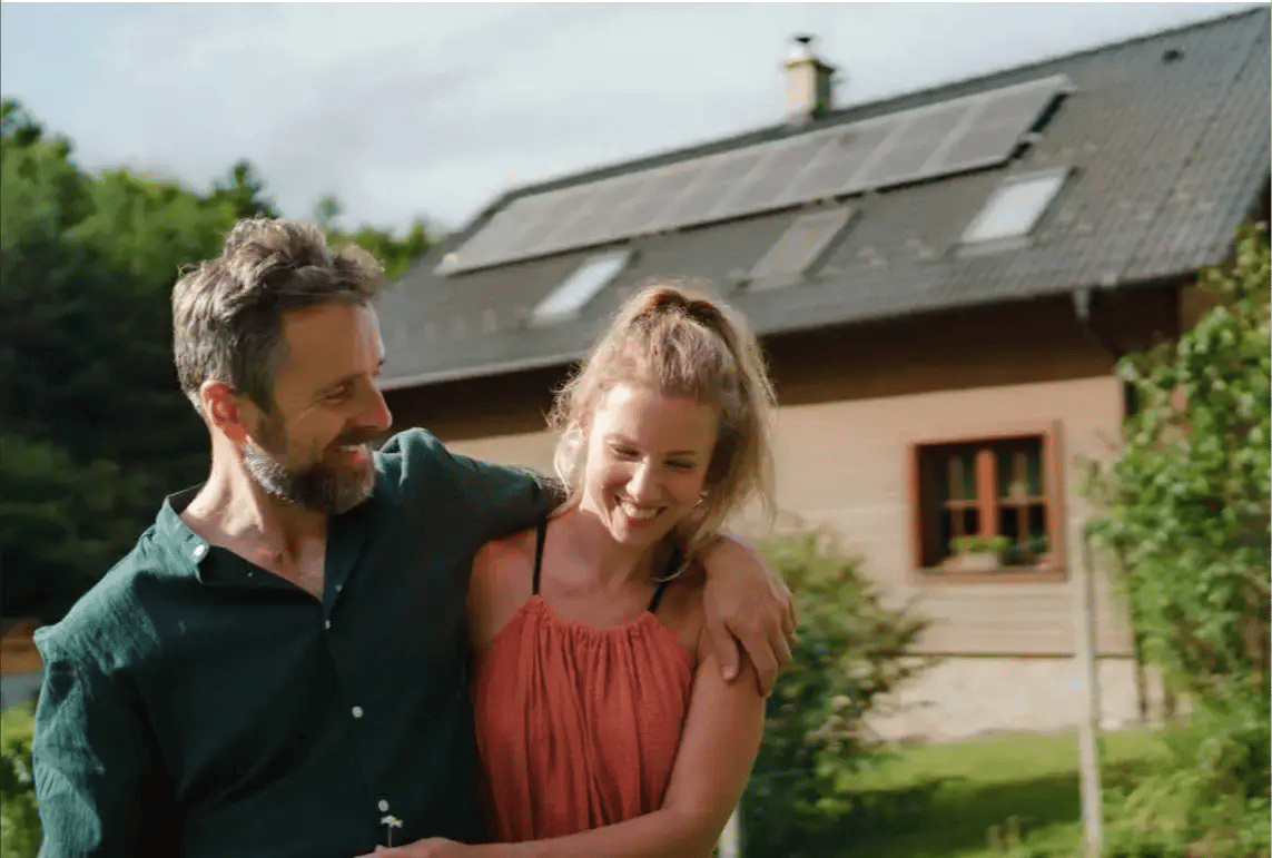 Mann und Frau umarmend im Garten vor Einfamilienhaus stehend mit PV Anlage am Dach